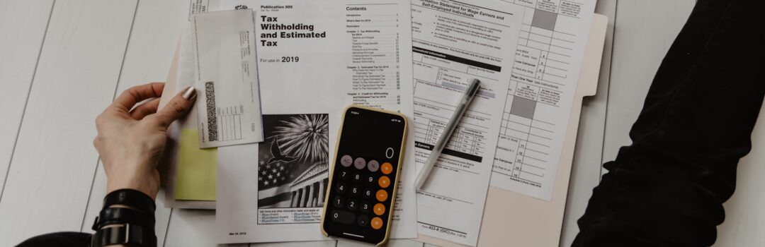 person holding paper near pen and calculator